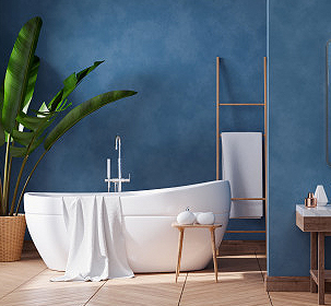 A modern bathroom with blue walls, a white freestanding bathtub, a towel draped over the edge, a wooden stool with bath accessories, a tall plant in a pot, and FL-inspired decor as sleek as garage doors Fort Meyers homeowners love.
