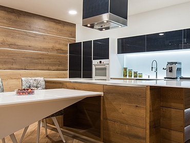 Modern kitchen with wood-paneled walls and cabinets, white countertop, built-in appliances, coffee machine, and a dining table for two. Located in FL, this space pairs style with convenience—much like the quality of garage doors Fort Meyers residents trust.