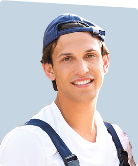 A young man smiling, wearing a white shirt, dark suspenders, and a blue baseball cap turned backwards, stands against a light blue background—ready to tackle garage doors in Fort Meyers, FL.