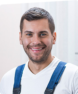 A smiling man with short brown hair and a beard, wearing a white shirt and blue suspenders, stands indoors against a light background in FL, possibly near garage doors Fort Meyers.